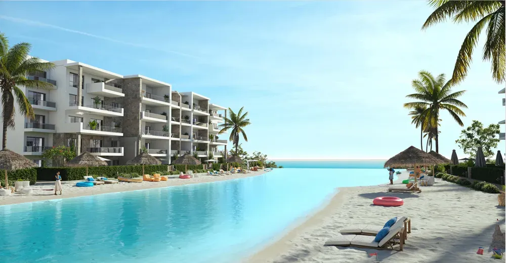 DOSE Al Dabaa lagoon beach Rendering of a sandy lagoon beach with sun loungers and residential buildings at DOSE, Al Dabaa